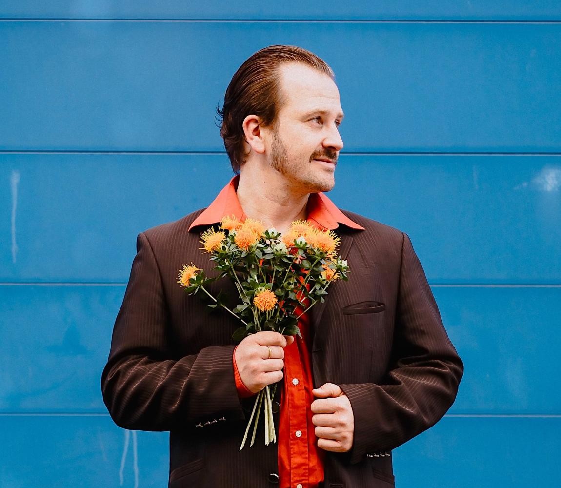 Ein Mann im Anzug und einem Blumenstrauß in der Hand guckt zur Seite