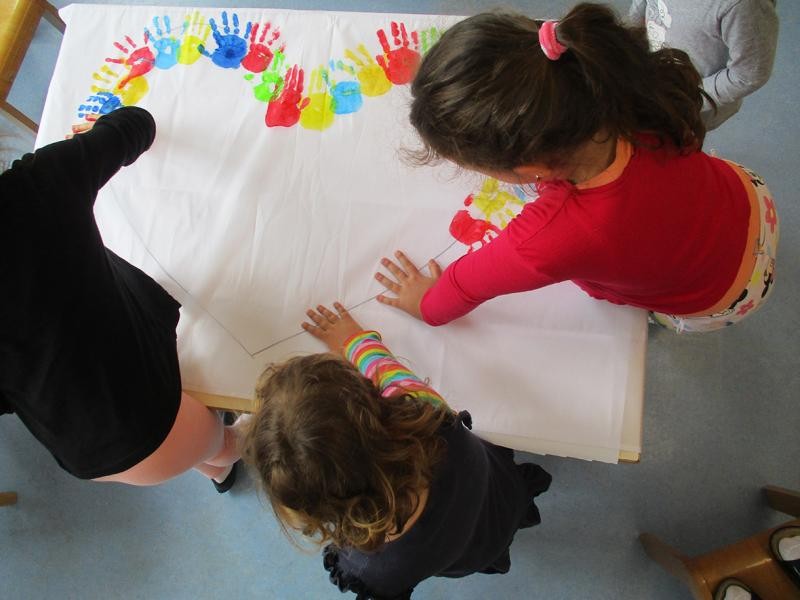 Kinder drücken bunte Hände auf ein großes Blatt Papier.