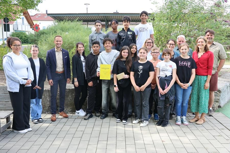 Erwachsene und Schüler stehen vor einem Grünstreifen und lächeln in die Kamera