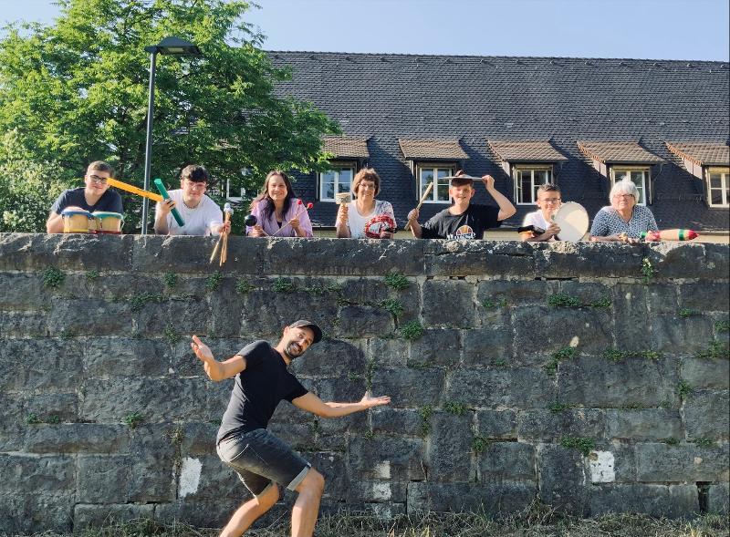 Personen schauen über eine Mauer, eine Person vor der Mauer im Vordergrund