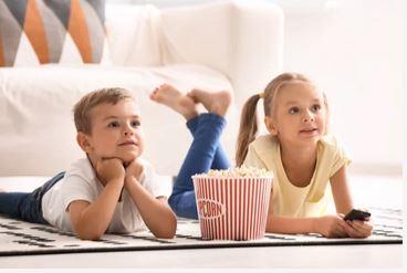 Kinder auf dem Boden mit Popkorneimer dazwischen und einer Fernbedinung in der Hand