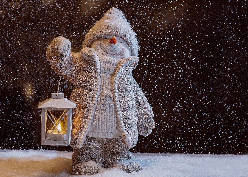 Schneemann mit Mütze, Jacke und Pullover sowie einer Kerze in der Hand