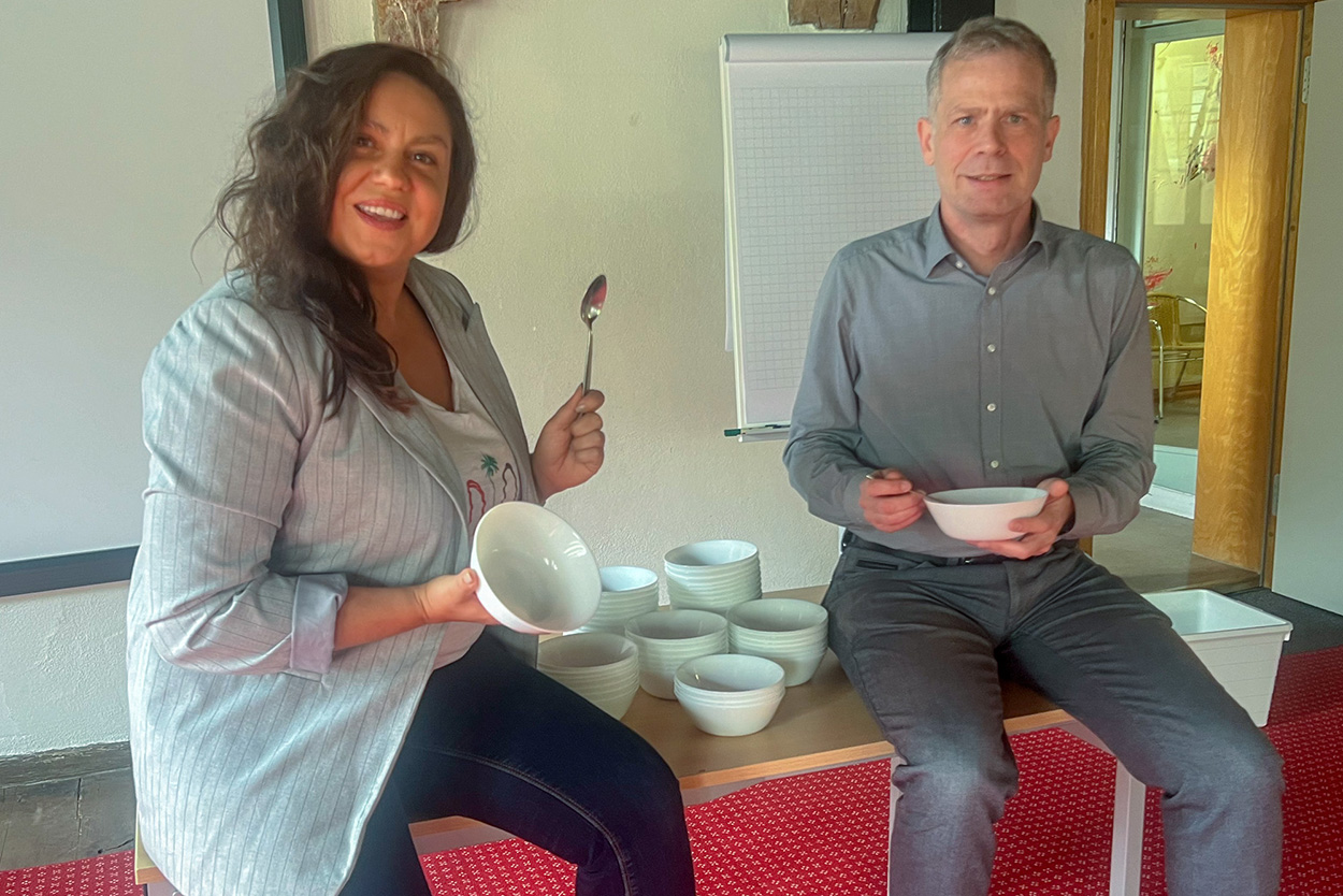 Eine Frau und ein Mann sitzen mit Schüssel und Löffel in der Hand auf einem Tisch