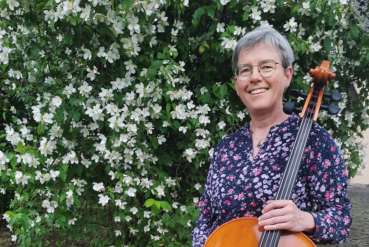 Eine Frau mit einem Cello steht vor einem blühenden Busch