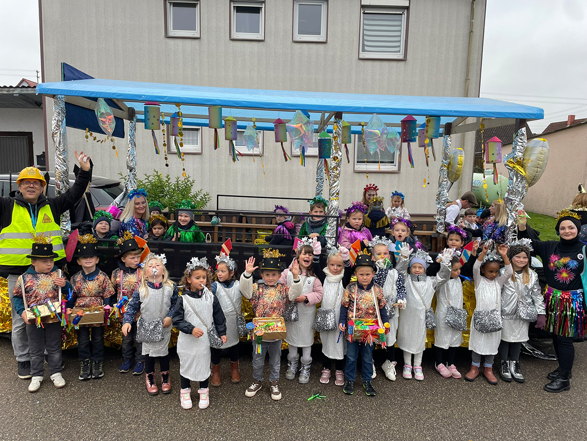 Viele Kindergartenkinder stehen mit ErzieherInnen vor einem bunten Umzugswagen