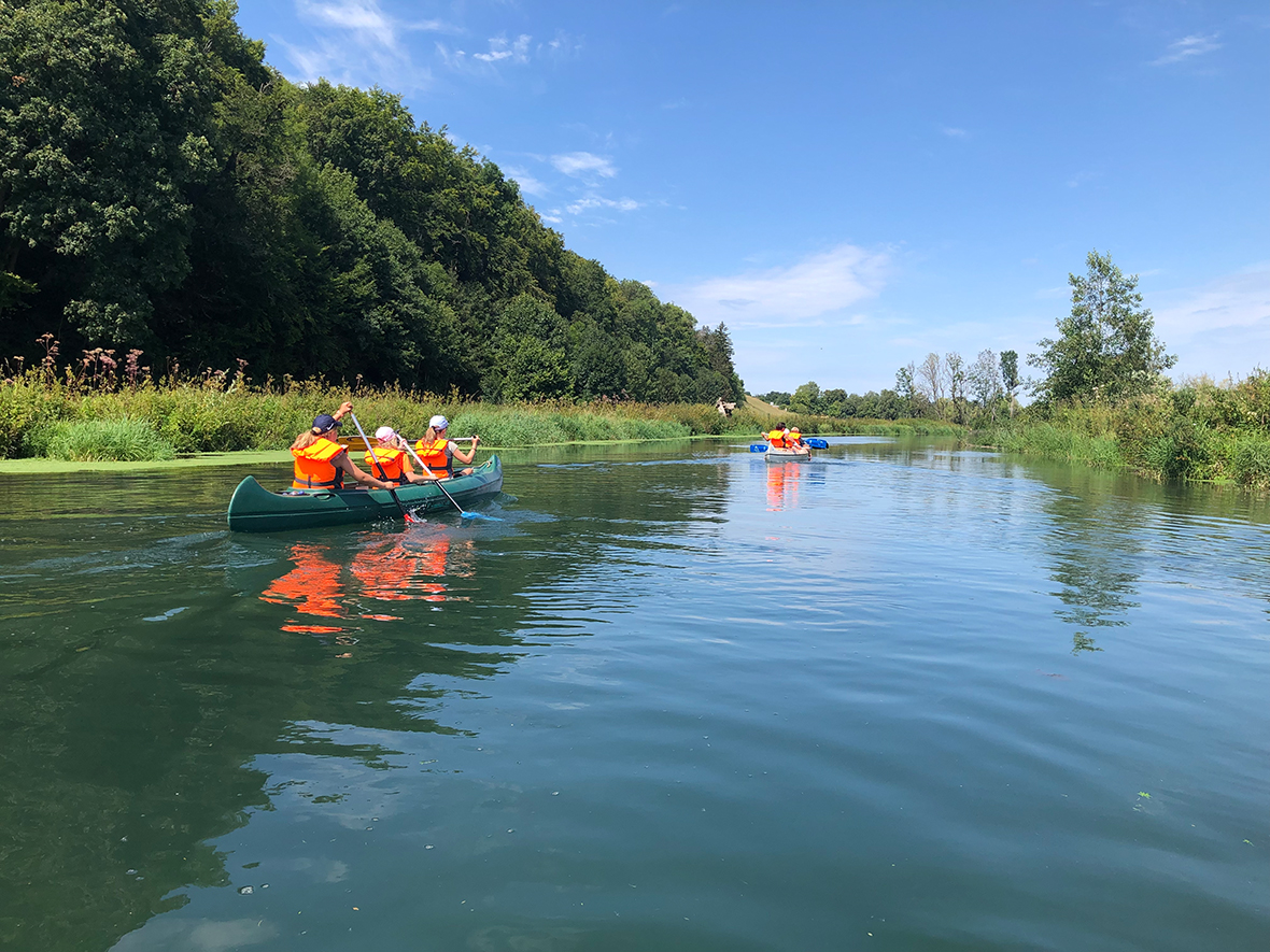 ein ruhiger Fluss auf dem zwei Knaus fahren, gesäumt von Wald und Wiesen,