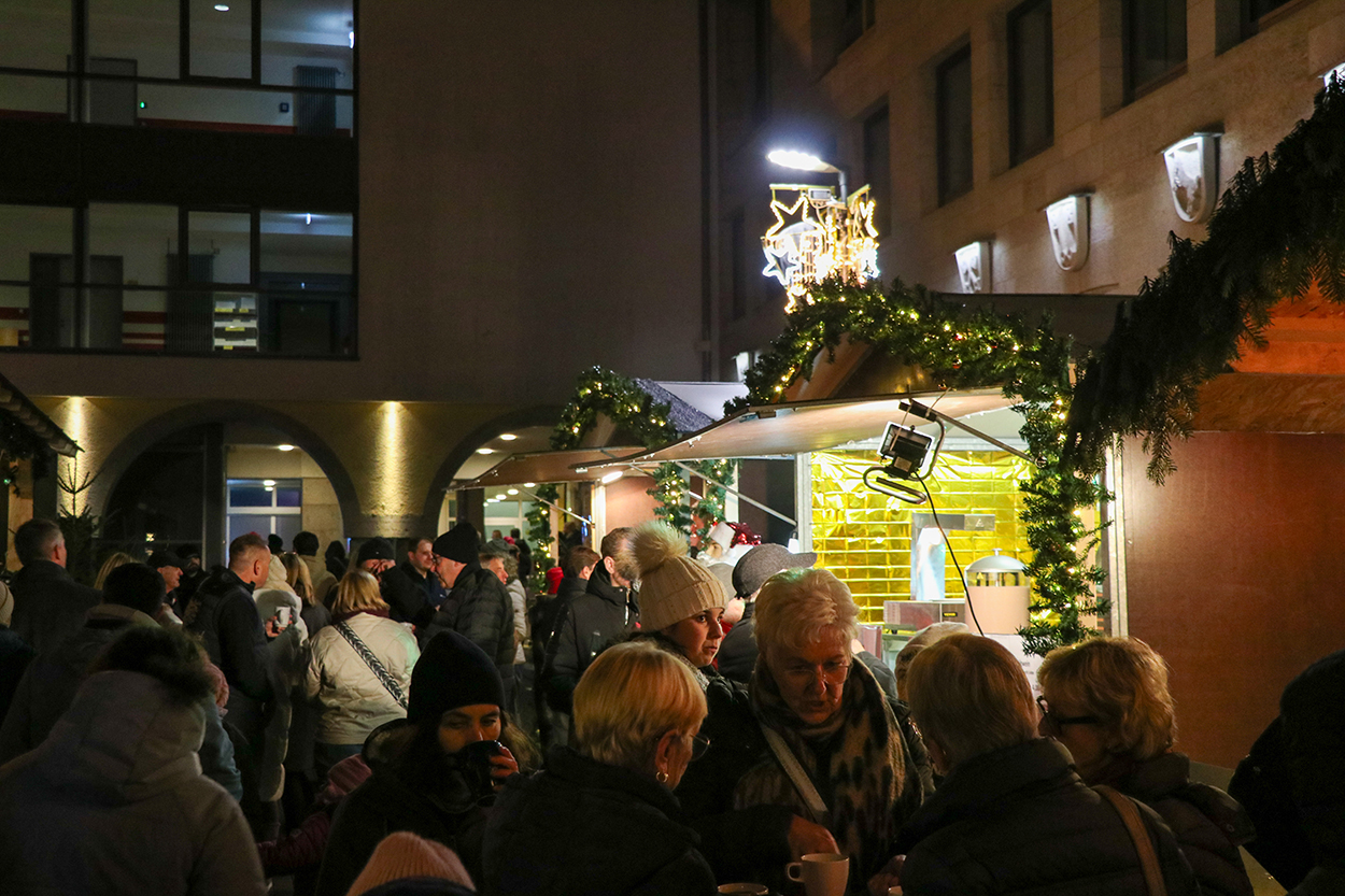 Viele Besucher auf einem leuchtenden Weihnachtsmarkt zwischen Buden