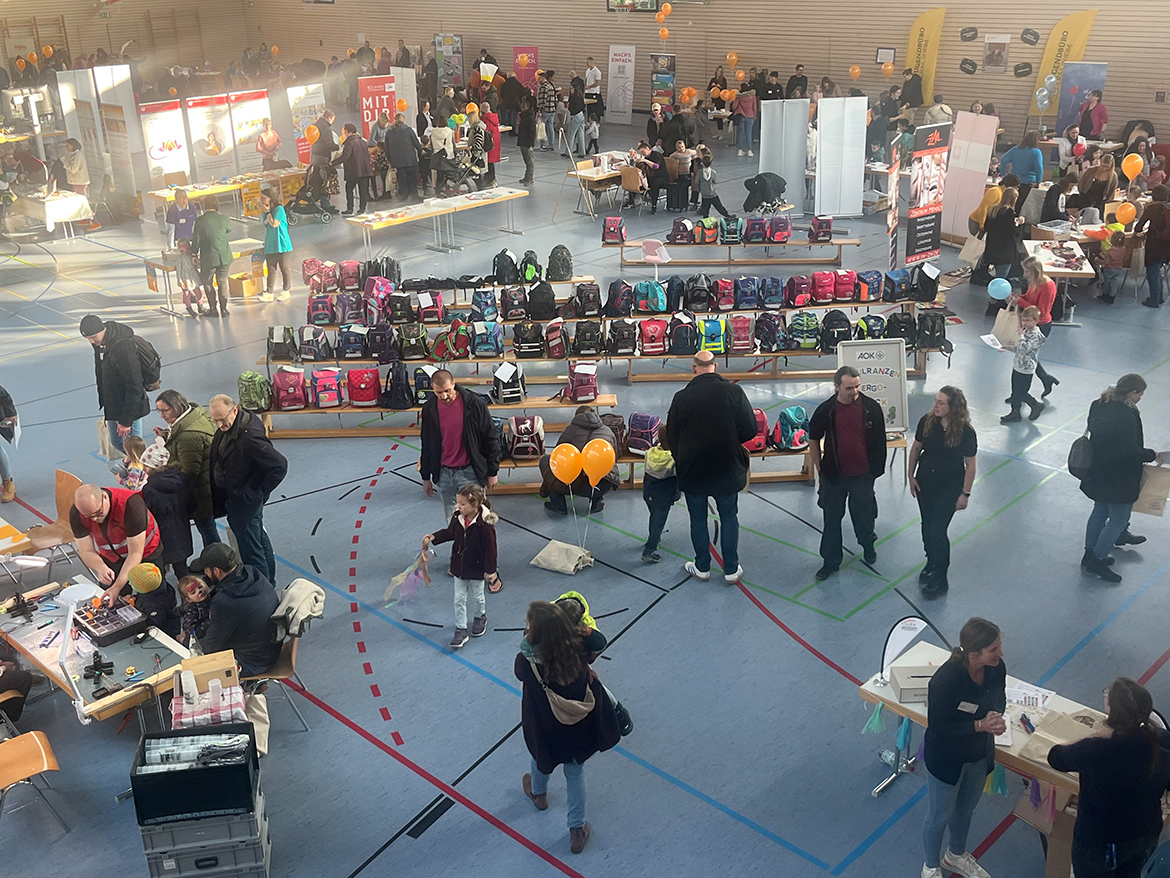 Viele Menschen an Tischen udn Ständen in einer Sporthalle