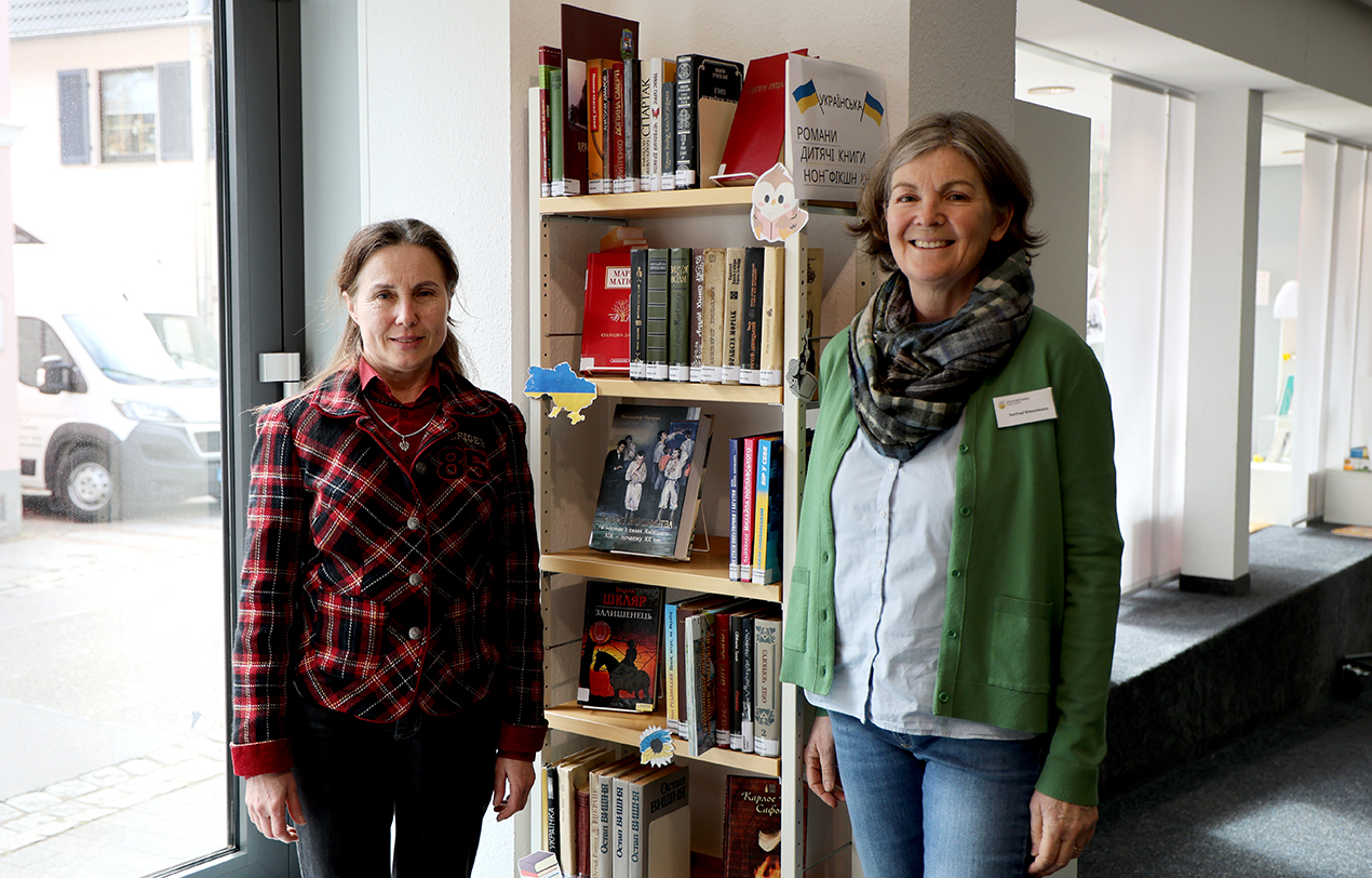 Zwei Frauen vor einem Bücherregal lächeln in die Kamera