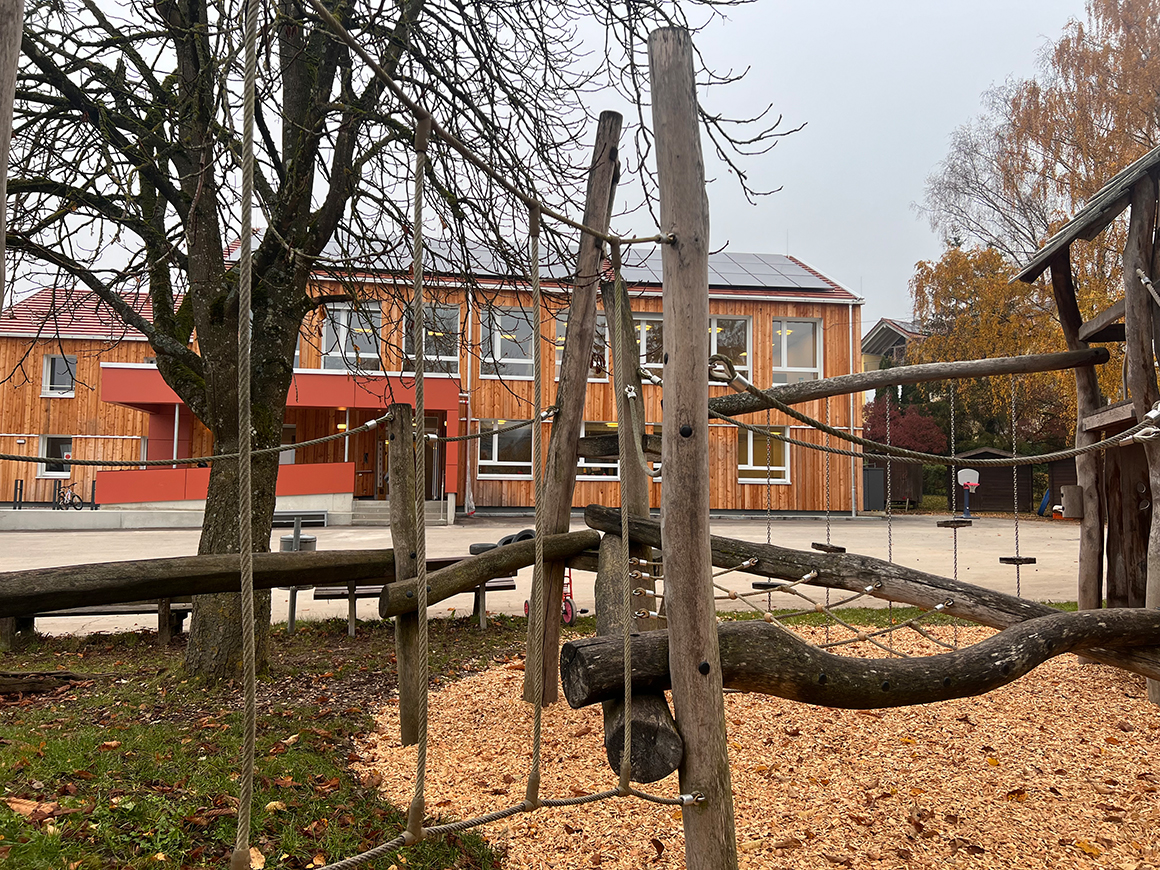 Ein Klettergerüst aus Holz, im Hintergrund ein Hof, dahinter ein Haus