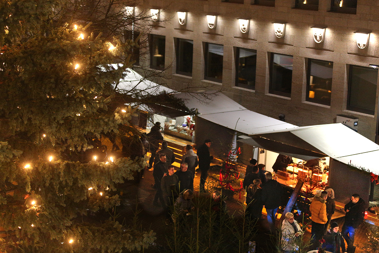 Ein beleuchteter Weihnachtsbaum, daneben Buden udn menschen