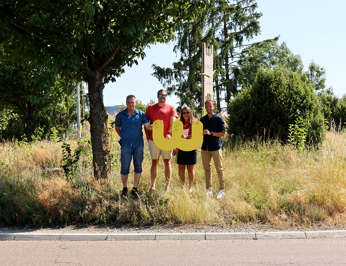 Drei Männer und eine Frau stehen auf einer Verkehrsinsel hinter einem großen gelben W