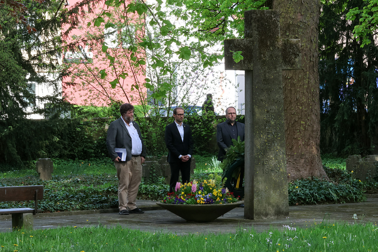 Drei Männer stehen vor einem steinernen Kreuz