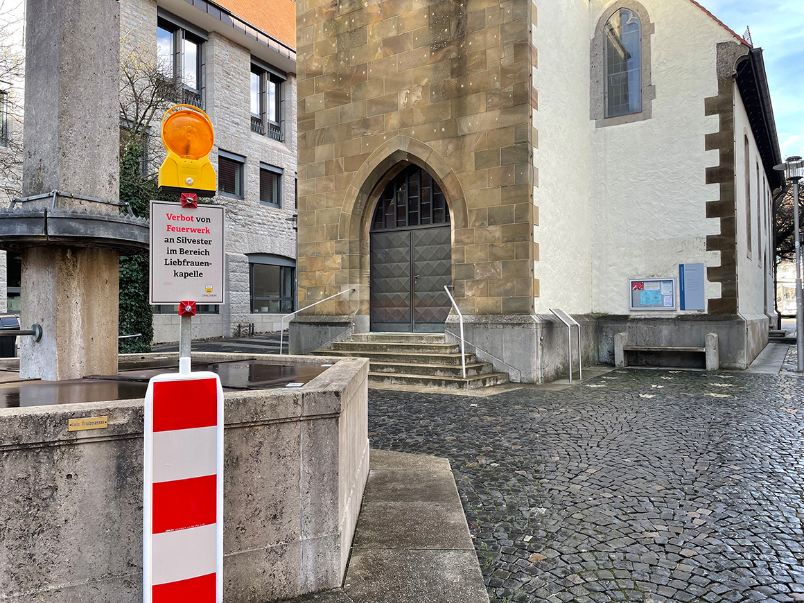 Eine weiß-rote Warnbarke mit Hinweisschild vor einem historischen Gebäude.