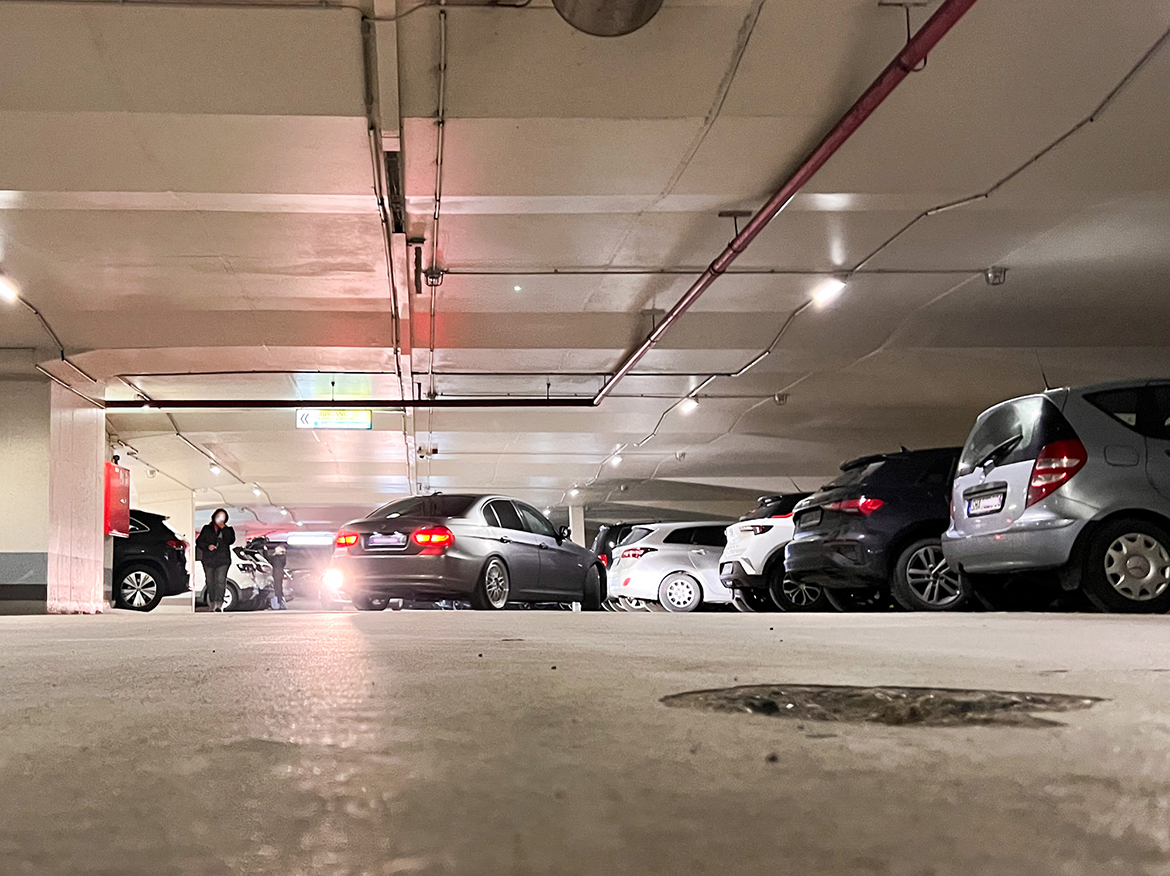 Eine Tiefgarage mit einigen Autos, eins parkt gerade aus, im Vordergrund ein kleiens Loch im Boden