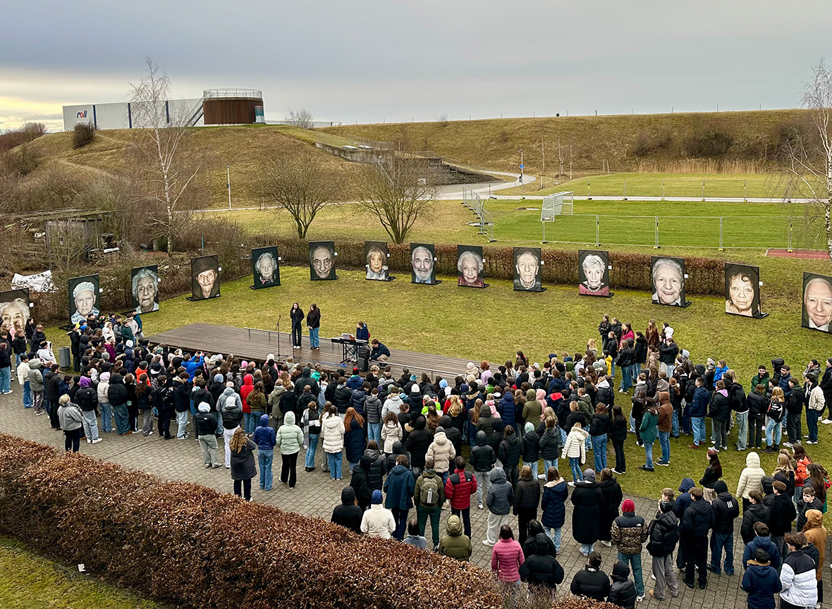 Viele Menschen stehen auf eienr Wiese um große Porträtfotos herum