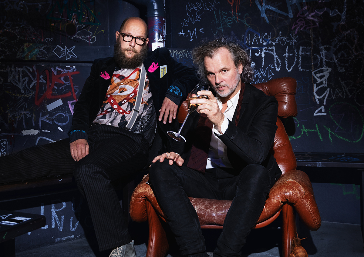 zwei Männer sitzen lässig in einer dunklen Kulisse