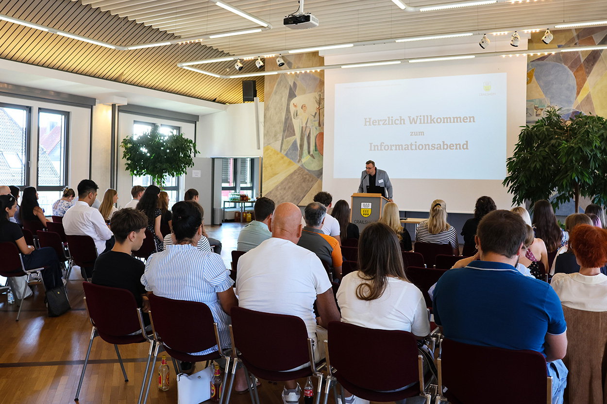 Ein Mann vor einer Leinwand am Rednerpult, davor ein Saal voller Menschen