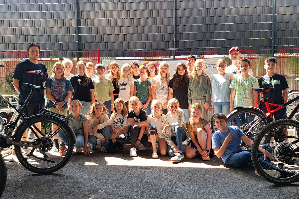 Ein Erwachsener und viele Schülerinnen und Schüler stehen in einem Radunterstand