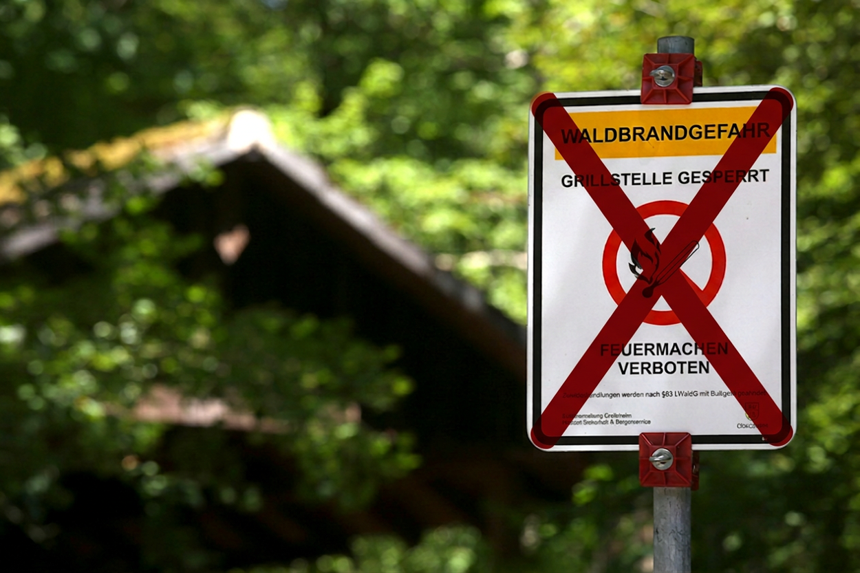 ein Verbotsschild, das durchgestrichen ist, im Hintergrund eine Grillhütte im Wald