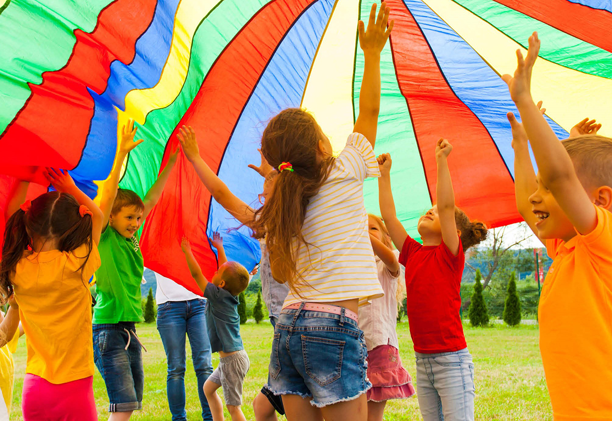 viele Kinder springen lachend unter einem Fallschirm