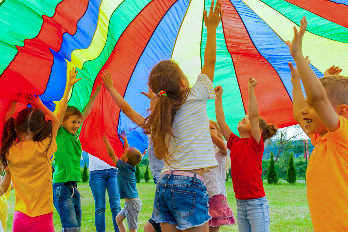 Kinder strecken sich fröhlich unter einem bunten Fallschrim