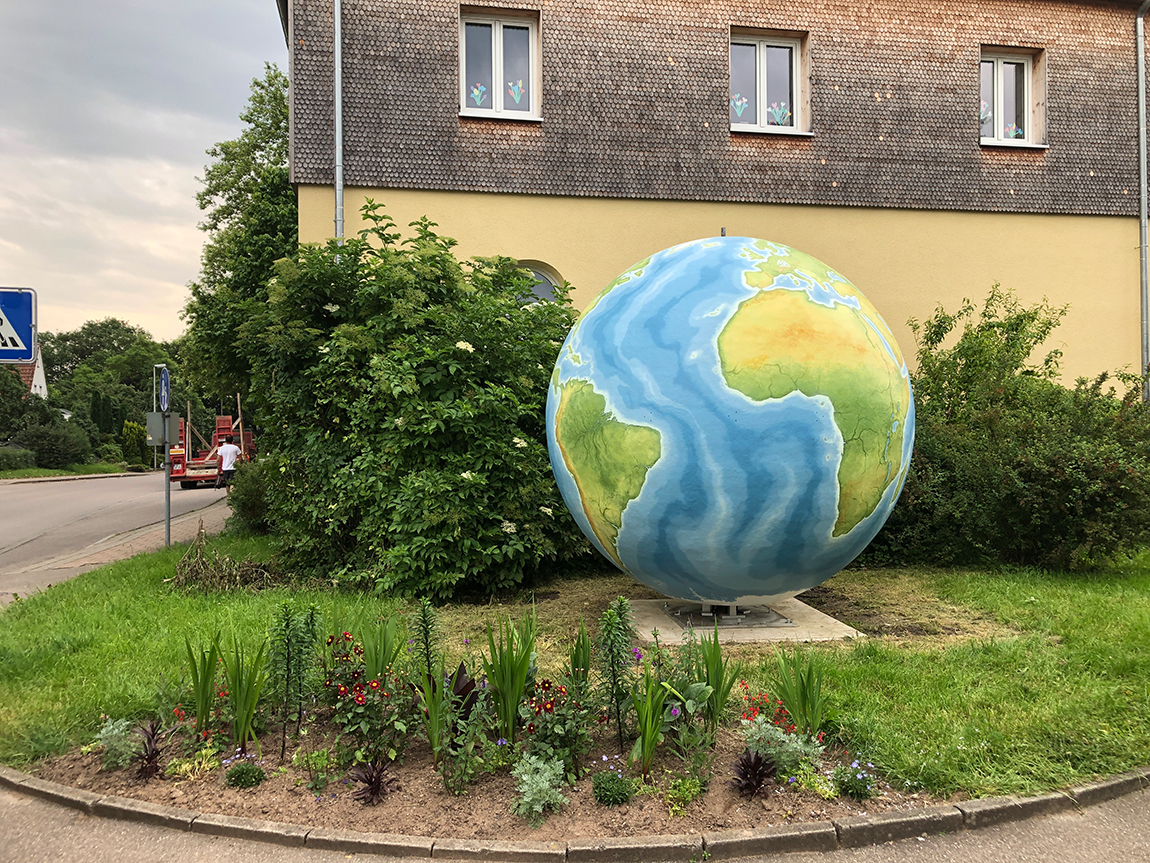 Eine riesige Weltkugel steht in einem Garten vor einem großen Haus