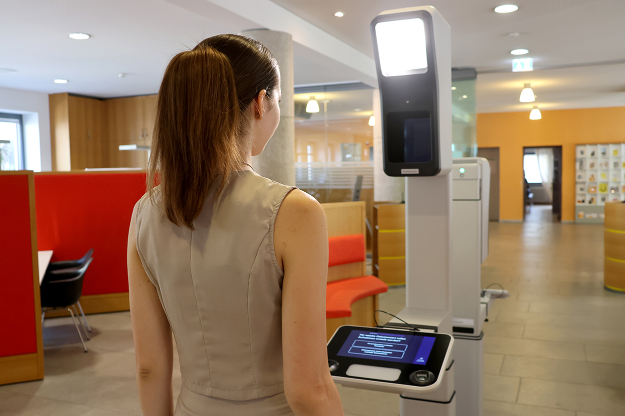 Eine junge Frazu steht vor einem Passfoto-Automaten in einem Bürgerbüro