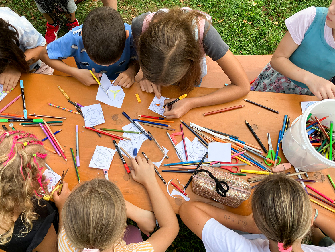 einige Kinder sitzen an einem Tisch mit vielen bunten Stiften und malen