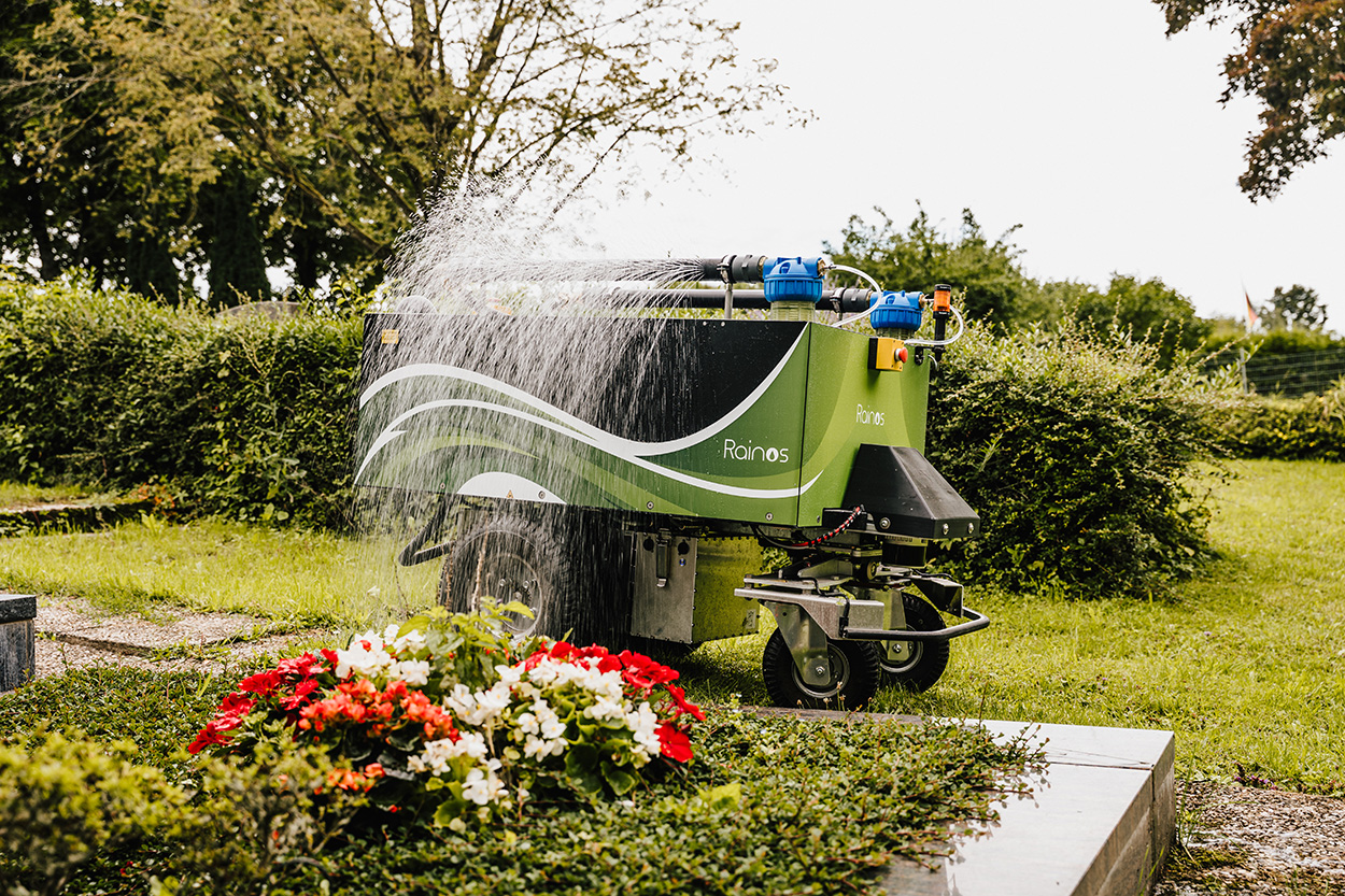 Ein großes Gefährt steht an einem Grab mit Blumen und gießt