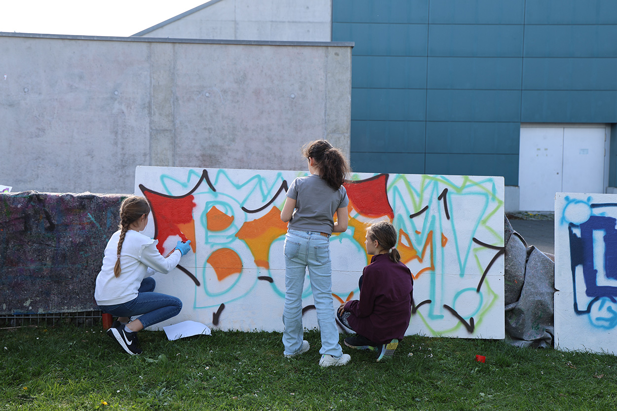 Drei Jugendliche sprayen auf eine große tafel.