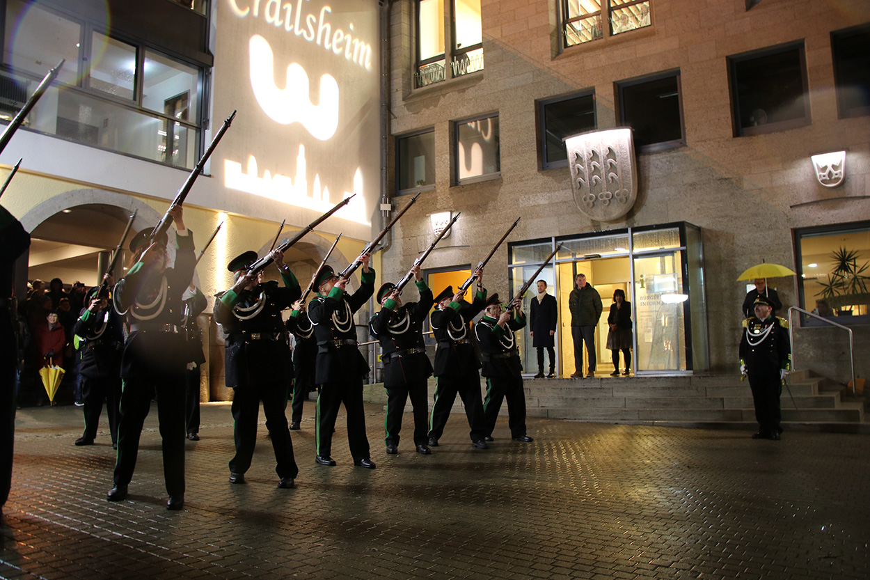 Mehrere Uniformierte vor dem Rathaus schießen Salut