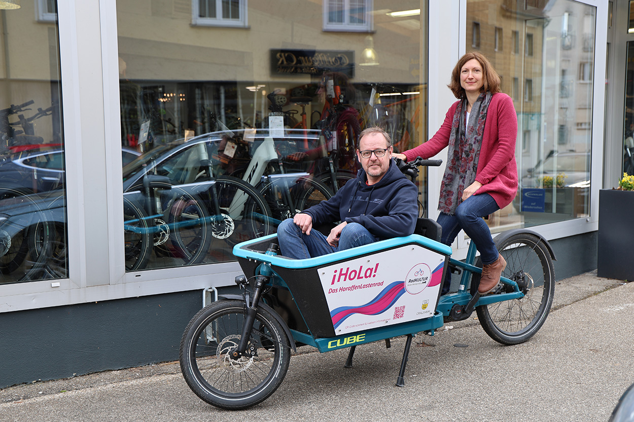 Ein Mann sitzt vorne in einem Lastenrad, eine Frau auf dem Sattel