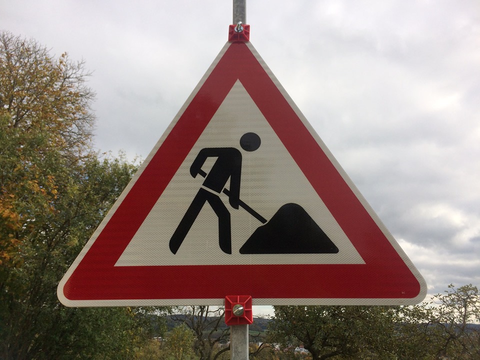 Ein Bastellenschild, dreieckig mit rotem Rad und einem Bauarbeitersymbol
