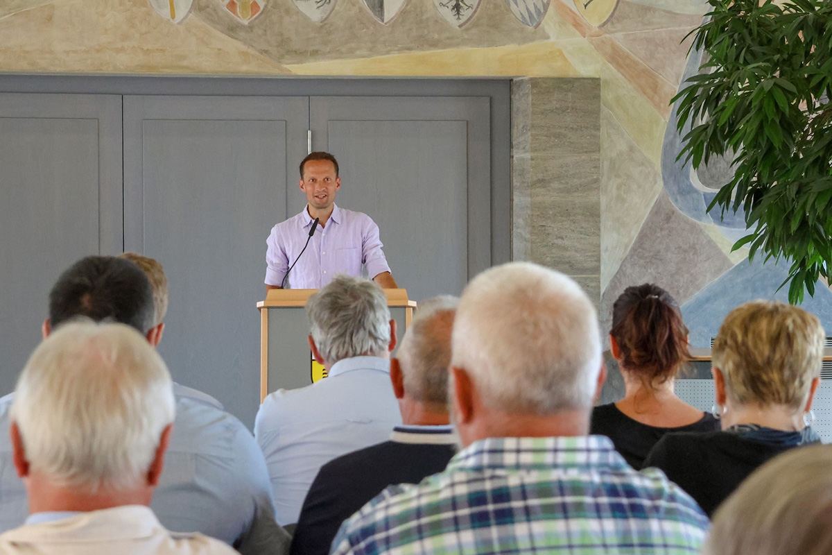 Ein Mann steht an einem Rednerpult, davor einige Zuschauer