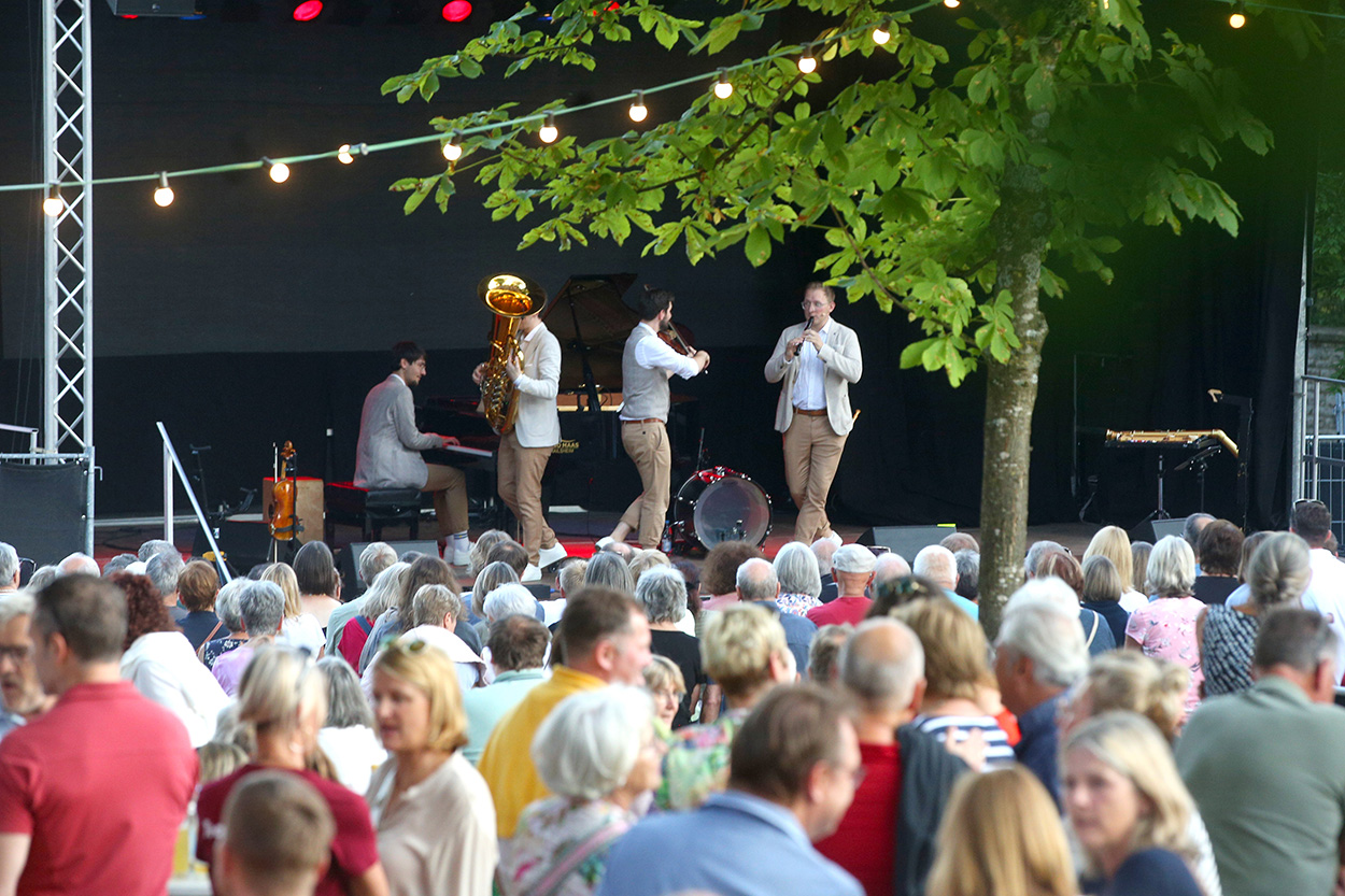Viele Menschen stehen vor einer Bühne, auf der eine Blasmusik-Band spielt.