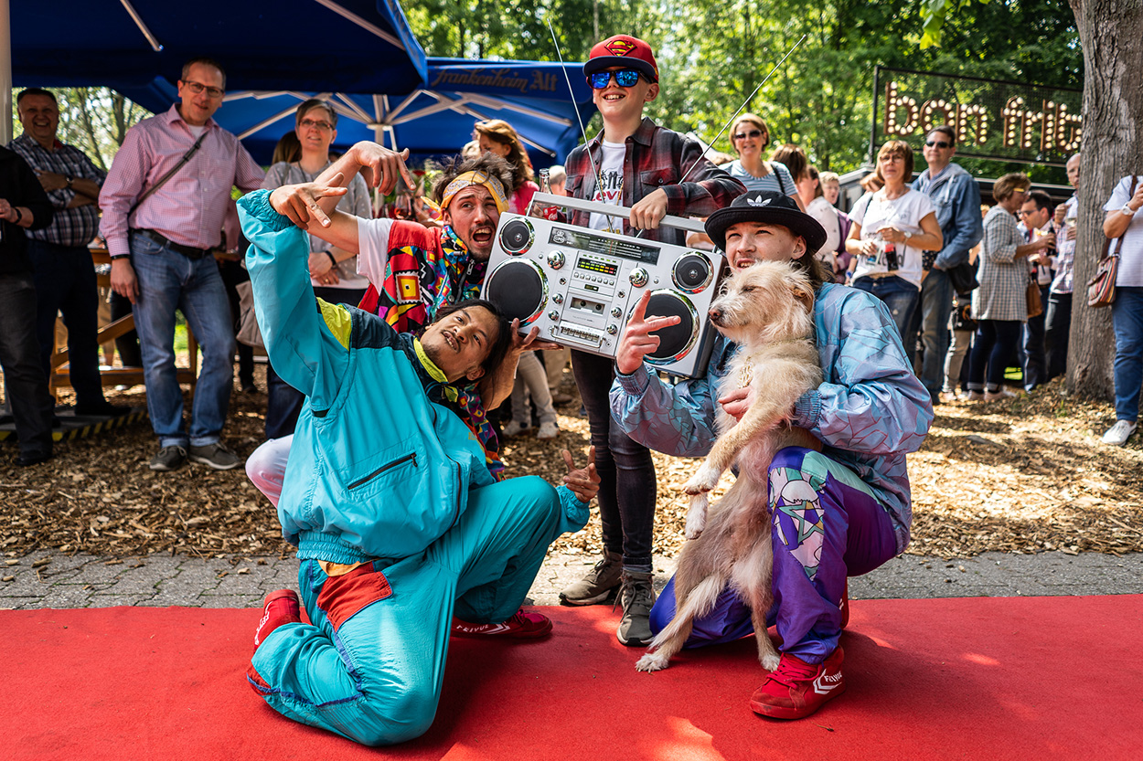 Eine bunte Truppe mit Ghettoblaster und Hund posiert für die Kamera