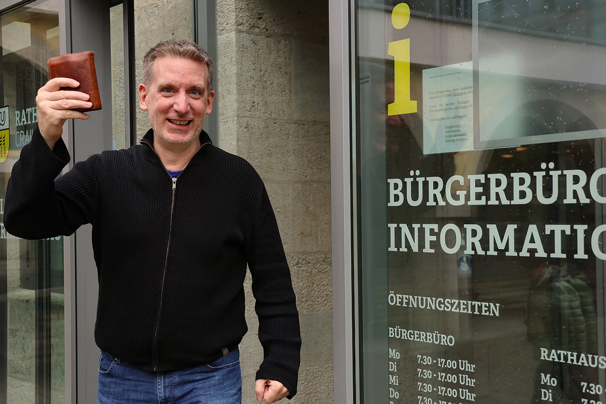 Ein Mann freut sich mit einer Geldbörse in der Hand vor einem Bürgerbüro