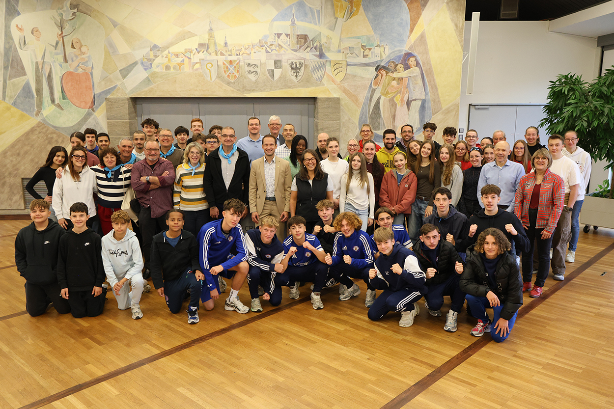 Eine große Gruppe sportlich gekleideter Menschen steht in einem Saal für ein Foto parat