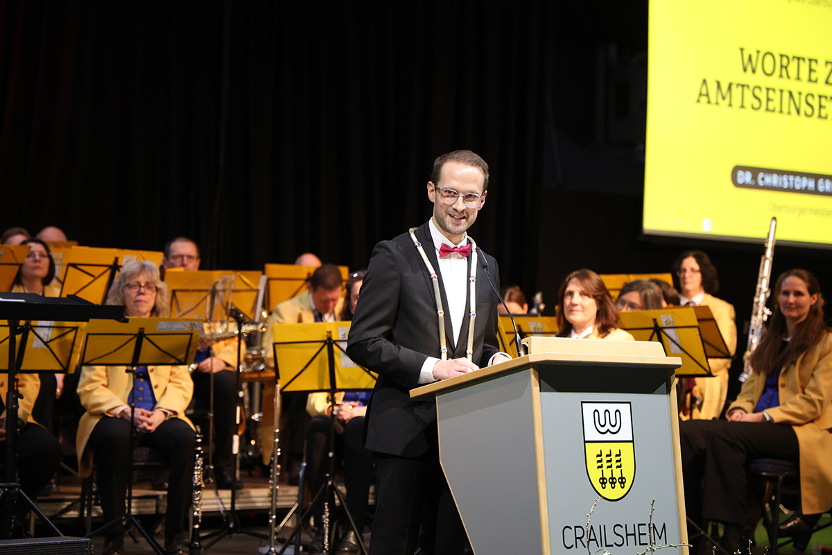 ein Mann steht an einem Rednerpult, dahinter ist eine Kapelle zu sehen