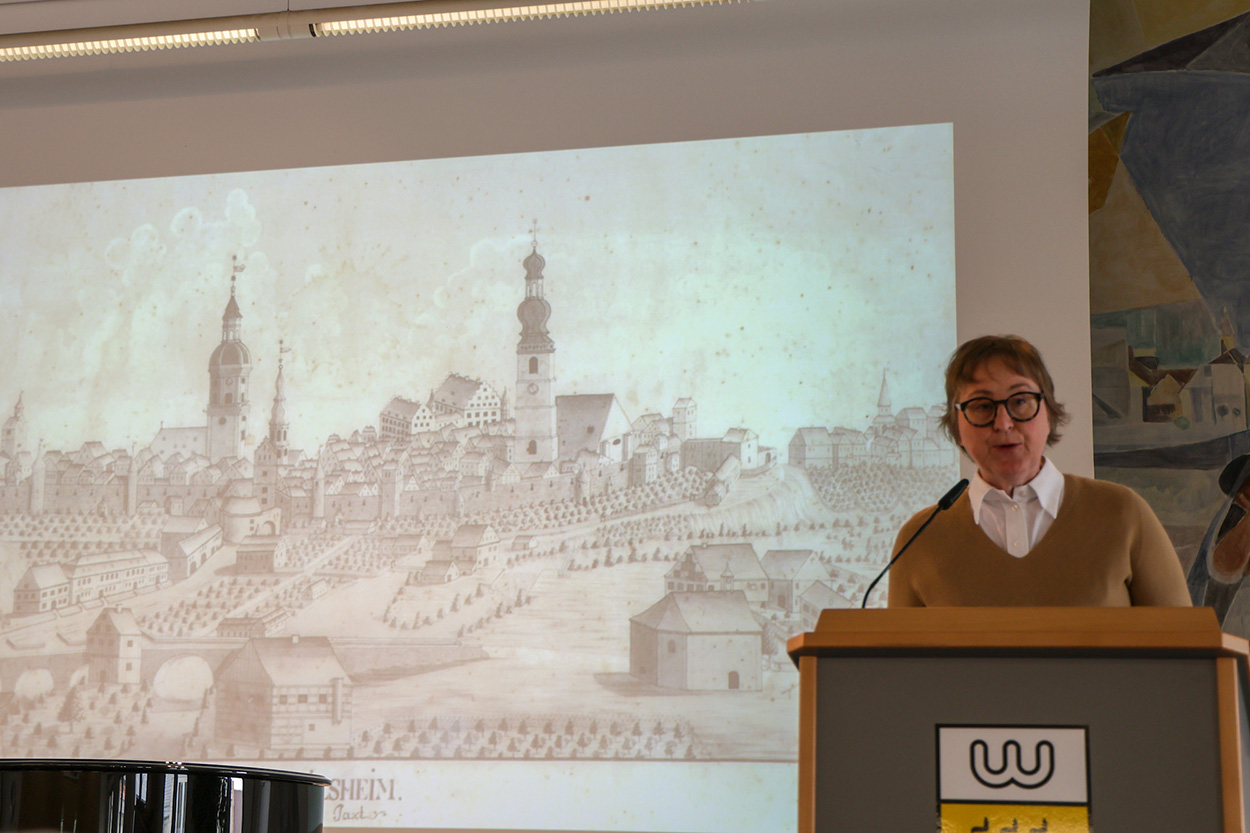 Eine Frau steht an einem Rednerpult vor einer Leinwand auf der ein historisches Bild Crailsheims zu sehen ist.