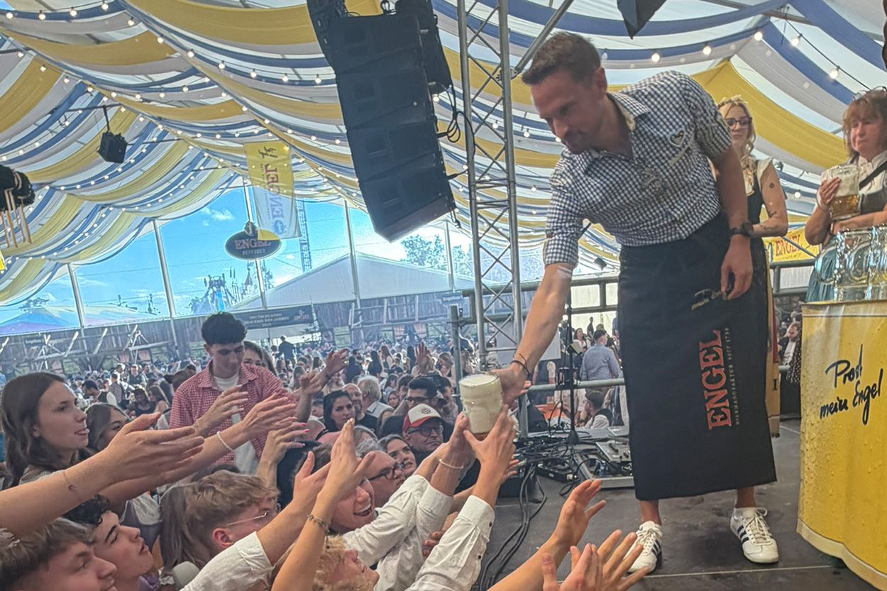 Ein Mann mit Brau-Schürtze verteilt Bier von eienr Bühne aus